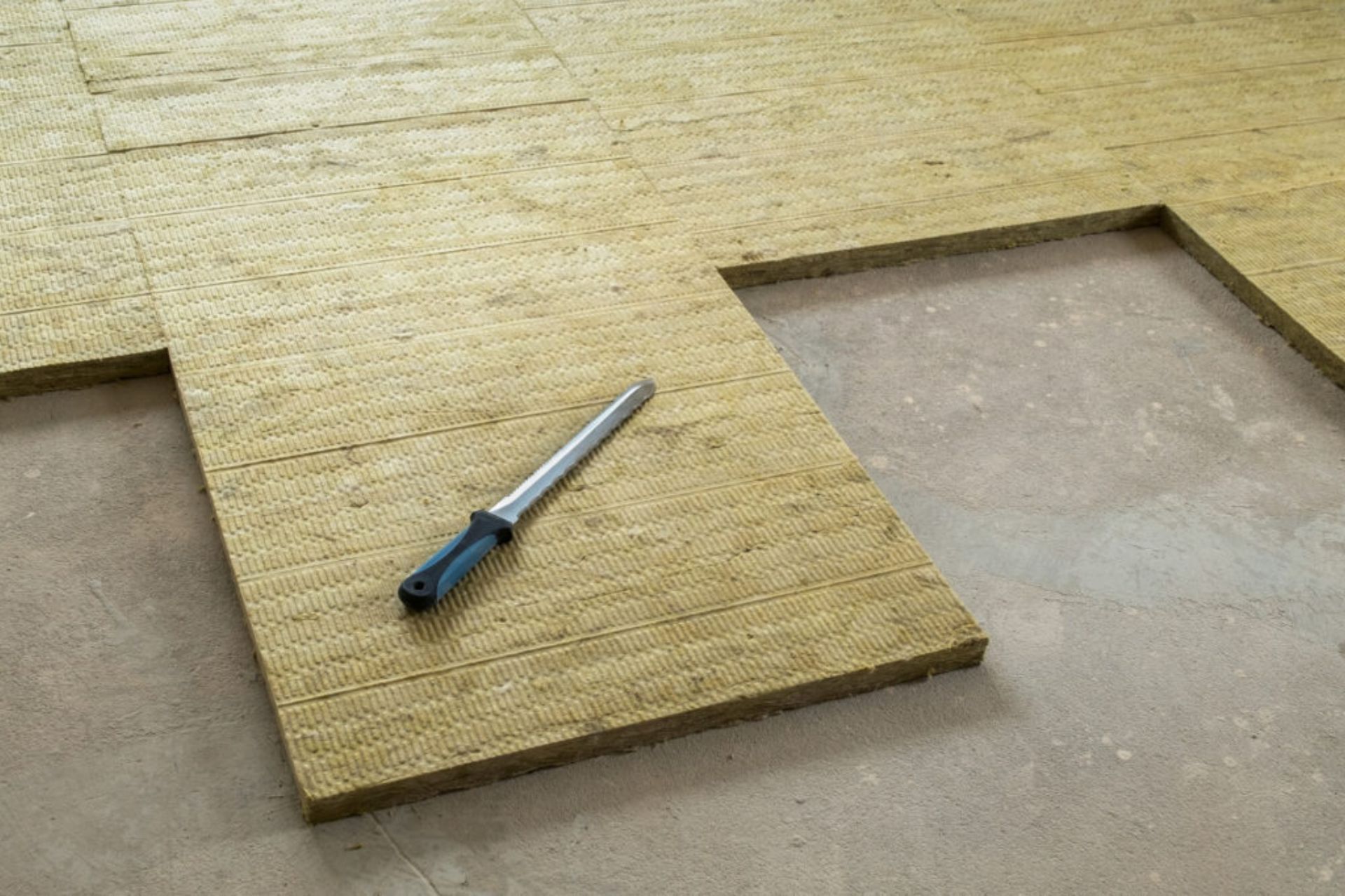 A partially installed floor made of textured panels, with a metal knife resting on top of one of the panels.