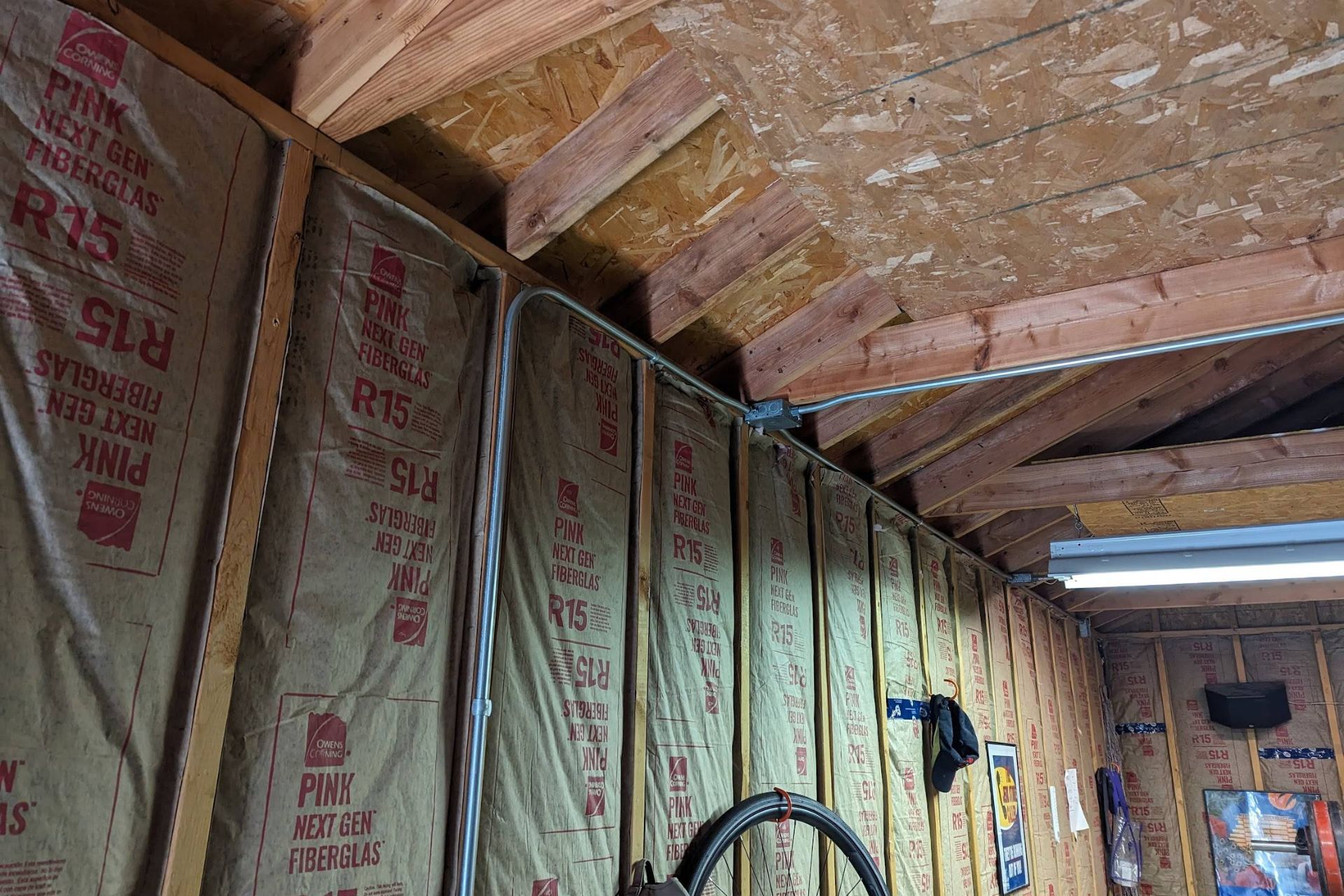 Interior of a garage featuring insulated walls, exposed wooden beams, and visible electrical wiring along the ceiling.
