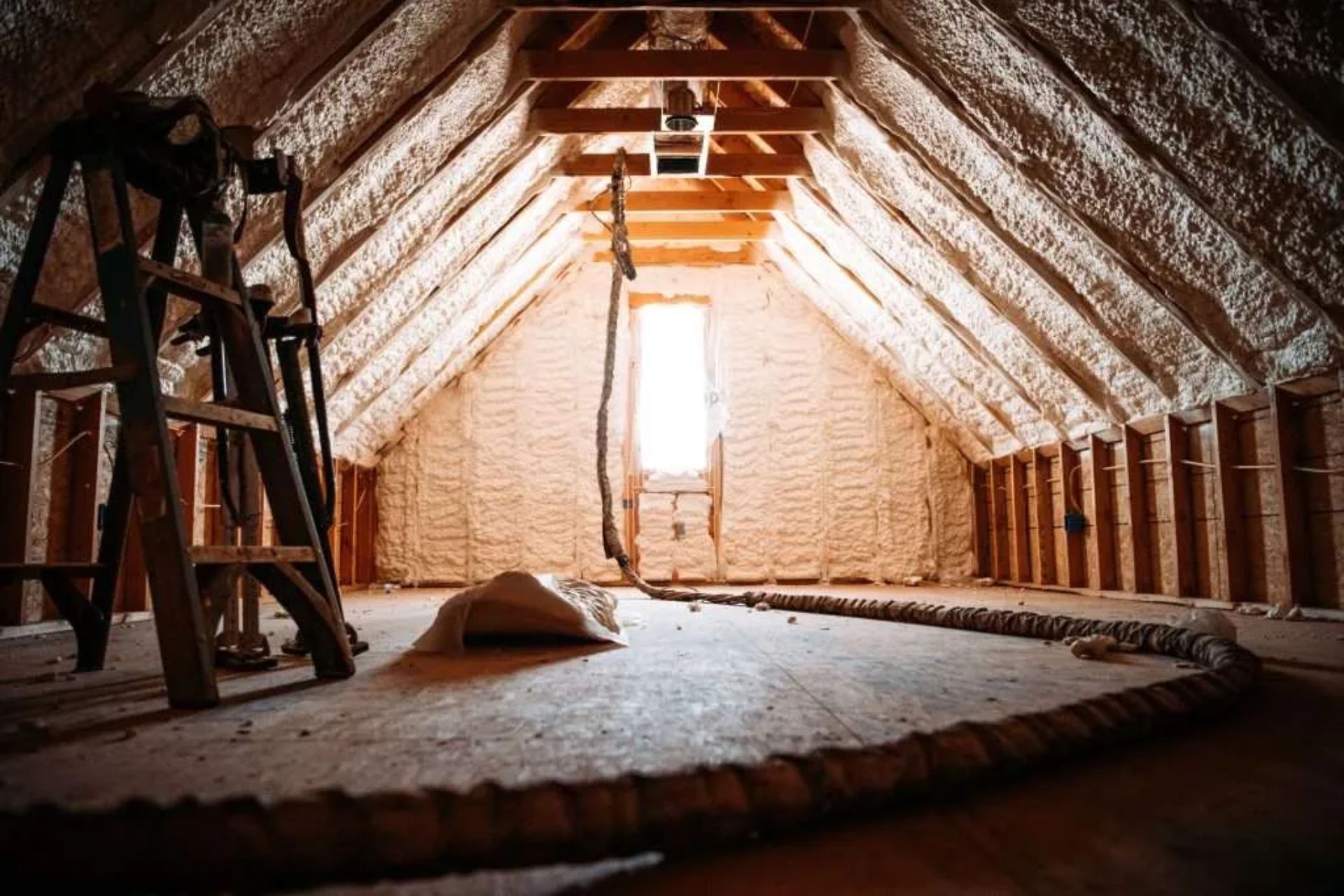 An attic space featuring exposed insulation materials, with wooden beams and a sloped ceiling visible in the background.