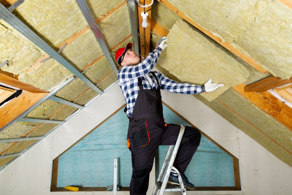 A man installs insulation on a roof, demonstrating an insulation service in progress.