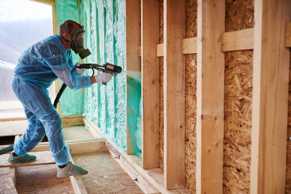 A man in a blue suit applies insulation spray to a wall as part of an insulation service.
