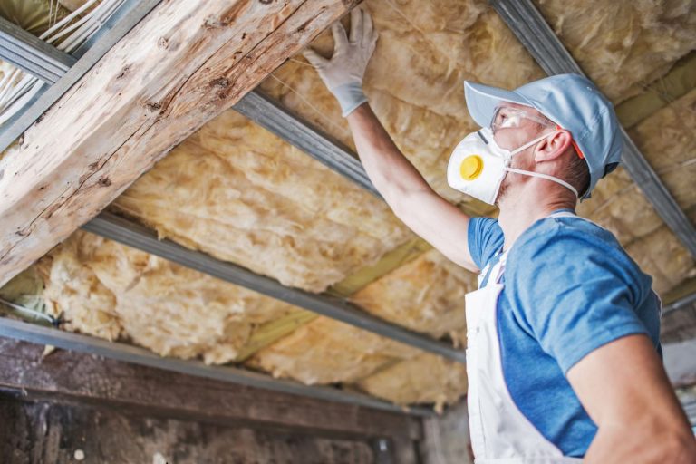 A man in a safety mask and gloves is repairing a ceiling, focused on his work in a well-lit room.