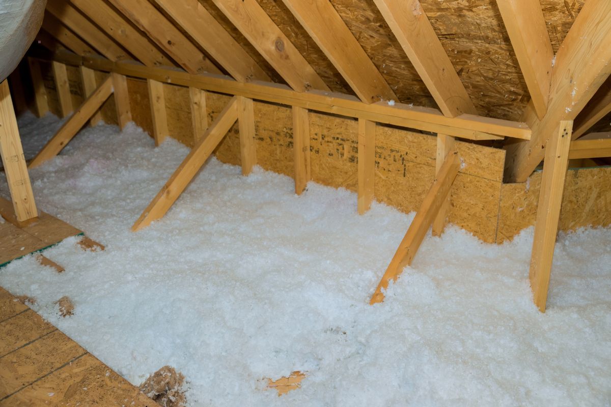 An attic space with exposed wooden beams and insulation material spread on the floor.